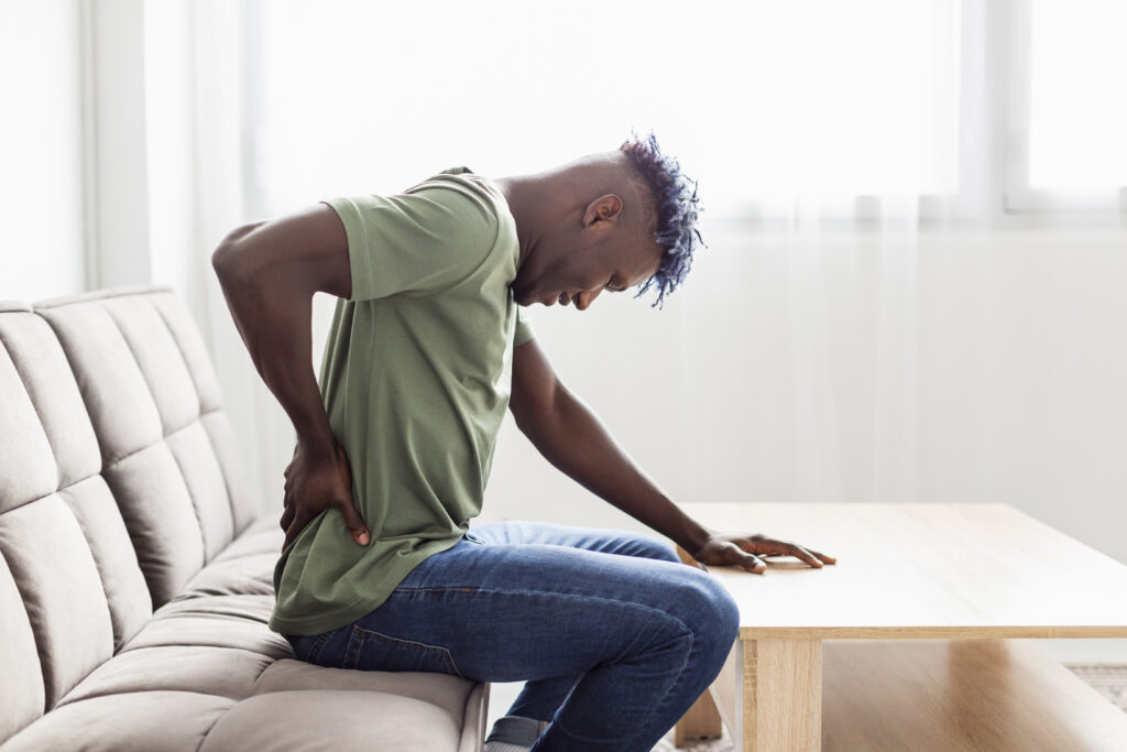 man sitting in couch holding her lower back pain