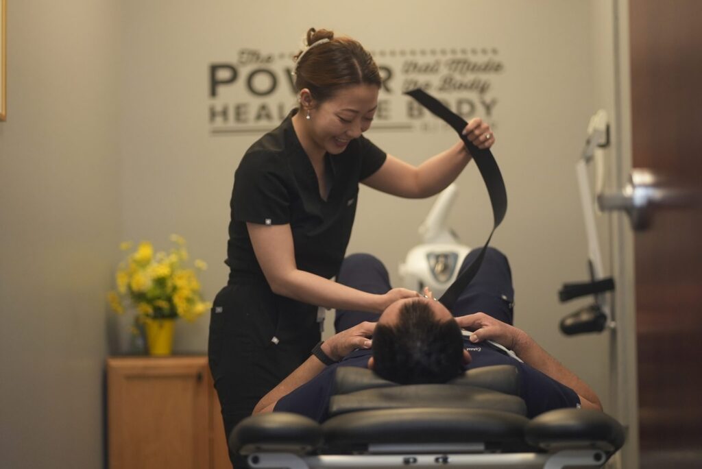 Chiropractor using an instrument tool to adjust a patient's neck while patient lies on treatment table